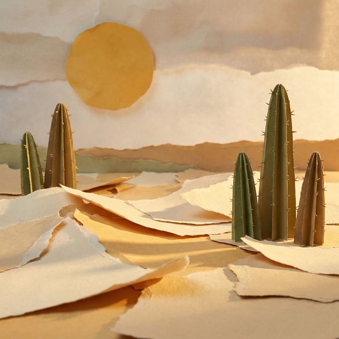Desert landscape sculpted entirely from torn paper — sand dunes made of ripped cream sheets with sof