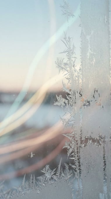 Ice crystals forming on a window pane, fractal patterns backlit by cold morning light