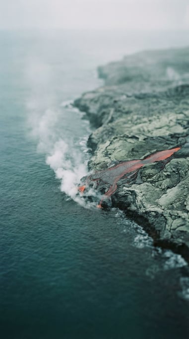 Lava flowing into ocean water, steam explosion at the contact point, red-orange meets dark blue