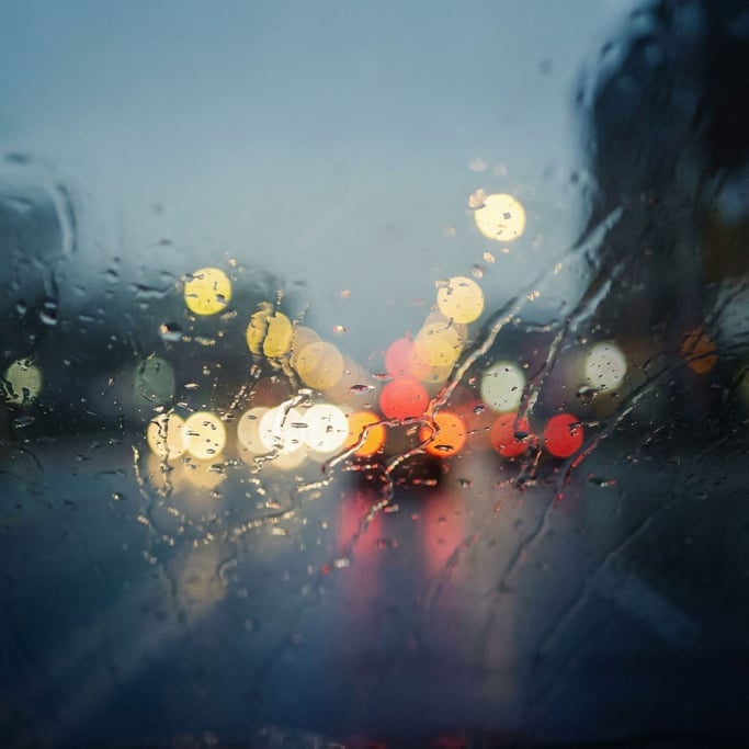 Rain on a car windshield at night, bokeh of city lights distorted through water droplets