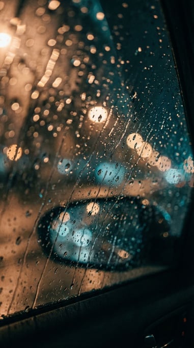Rain on a car windshield at night, bokeh of city lights distorted through water droplets (u)