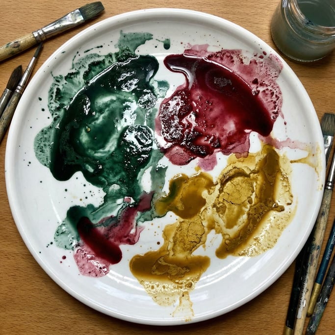 Concentrated pools of viridian green and alizarin crimson and yellow ochre spread across a glossy wh