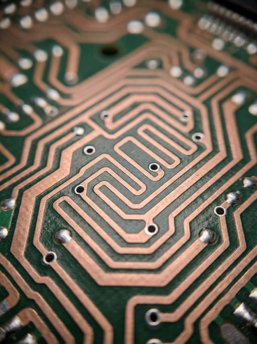 Copper pathways snake across dark green fiberglass substrate — circuit board traces magnified to abs