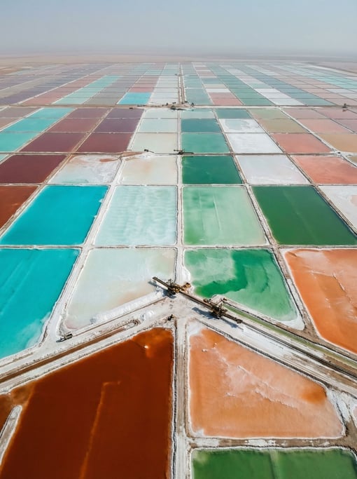 Geometric rectangular pools in varying stages of evaporation create a patchwork of vivid unreal colors — aerial view of salt evaporation ponds