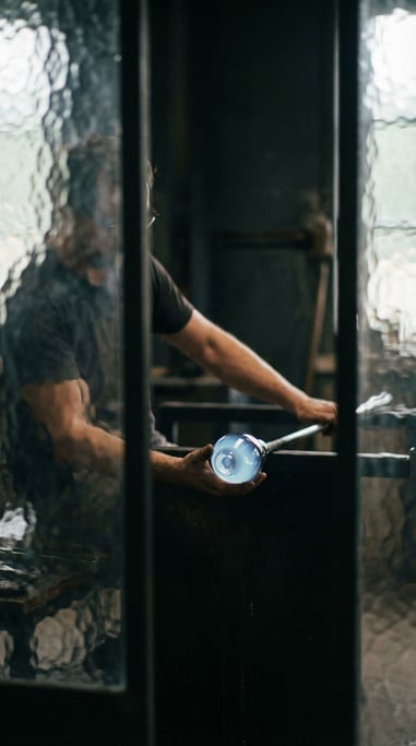Molten glass being shaped by a glassblower, glowing blue-white against a dark workshop (etuuuz)