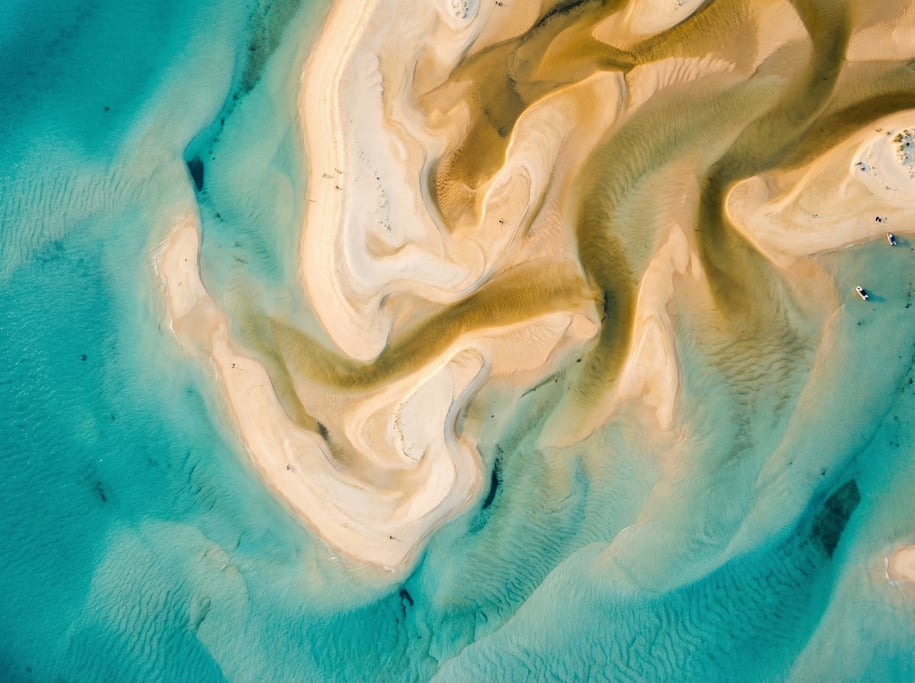 Drone view of sandbar formations at low tide creating abstract organic shapes in cream and gold