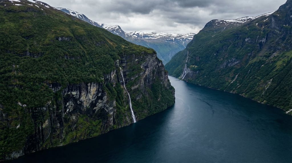 Wide aerial panorama of a dramatic fjord with steep dark green cliffs dropping into deep navy blue w
