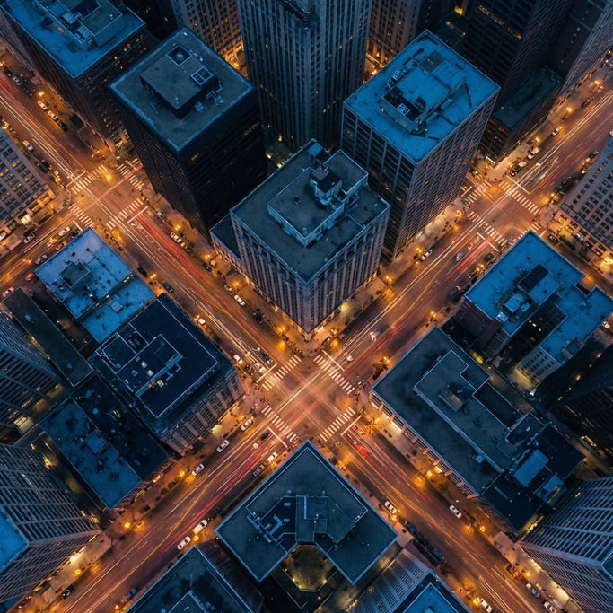 Overhead drone shot of a dense urban intersection at blue hour with warm amber streetlights