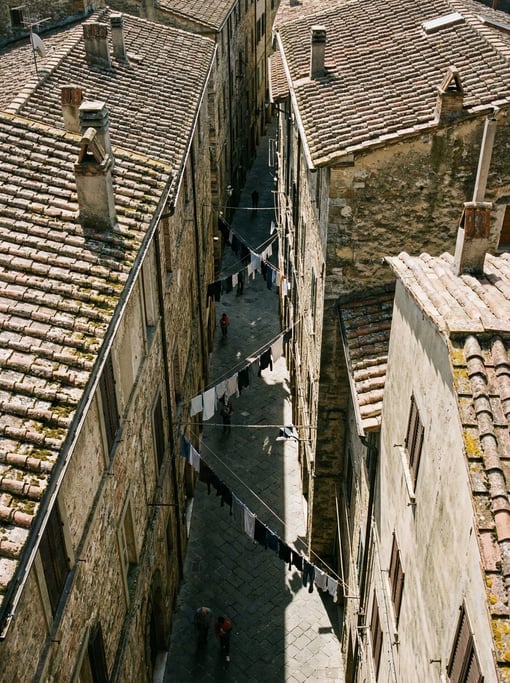 Top-down aerial of a narrow European alley between tall buildings with terracotta roofs