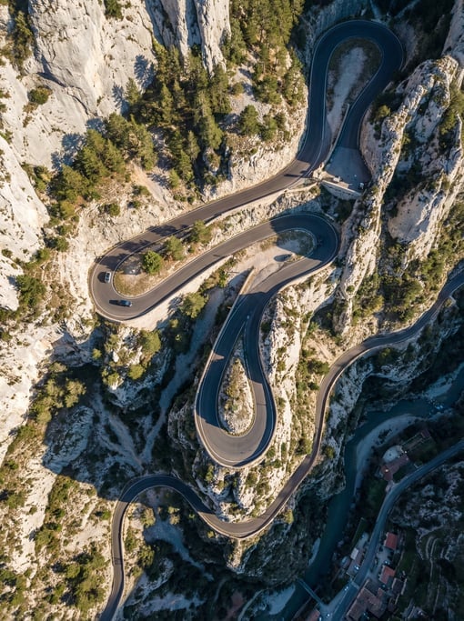 Top-down drone view of a winding mountain road with tight switchback hairpin turns carved into grey