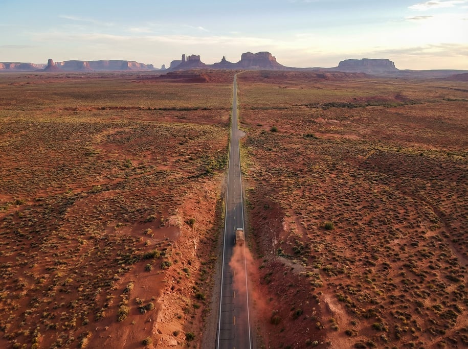 Drone view of a long straight desert highway cutting through flat red mesa terrain