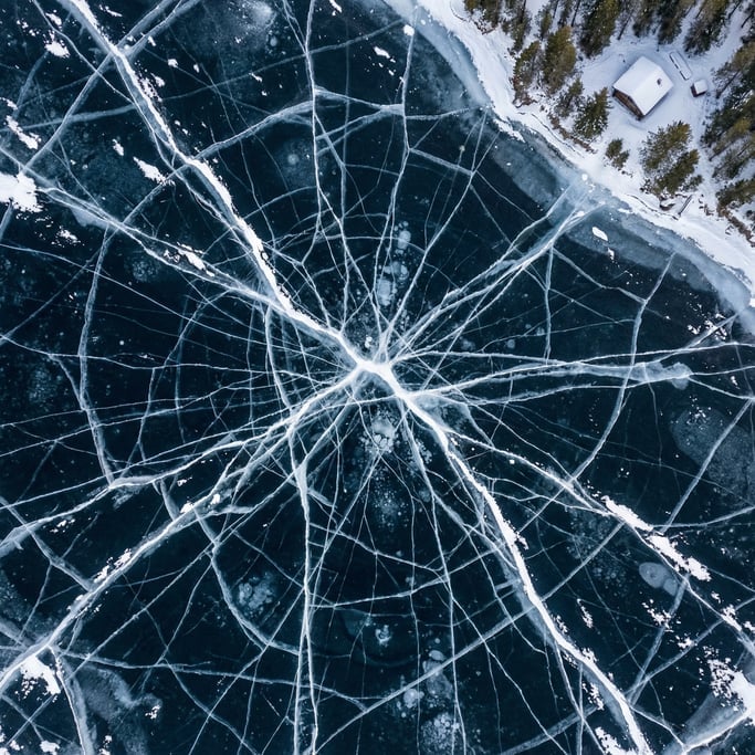 Overhead aerial of a frozen lake with natural ice crack patterns radiating from the center
