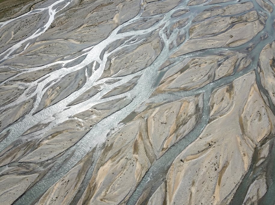 Top-down view of a braided river channel with multiple streams weaving through pale gravel bars