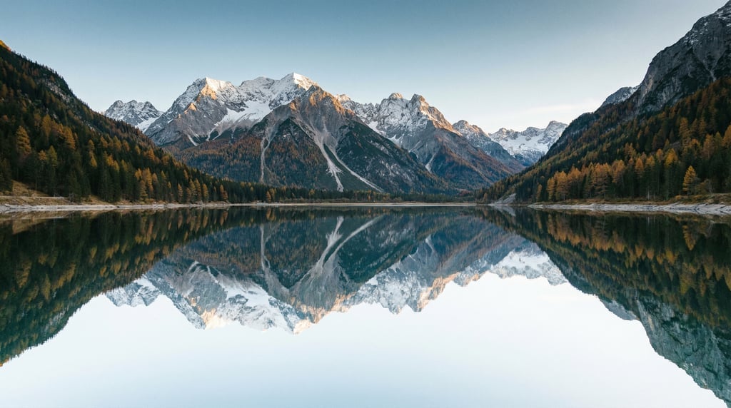 Wide aerial of a still mountain lake reflecting snow-capped peaks in perfect mirror symmetry