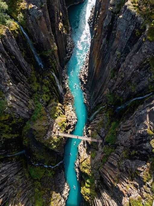 Drone view of a narrow gorge with a turquoise river flowing between steep dark rock walls