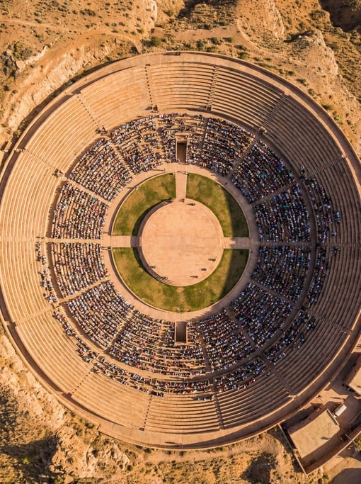 Overhead aerial of a large outdoor amphitheater with concentric curved concrete seating rows creatin