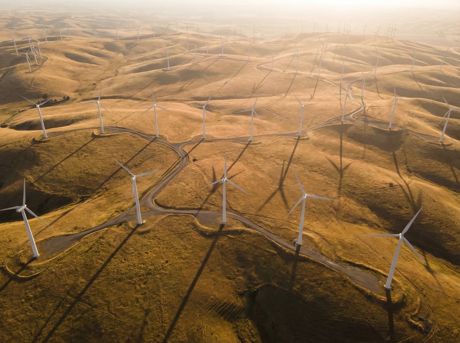 Aerial view of a wind farm from above with white turbines scattered across golden hills