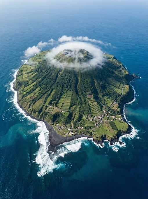 Top-down aerial of a volcanic island rising from deep blue ocean, lush green slopes