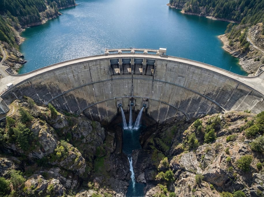 Aerial shot of a dam wall from above showing the curved concrete face holding back a full reservoir