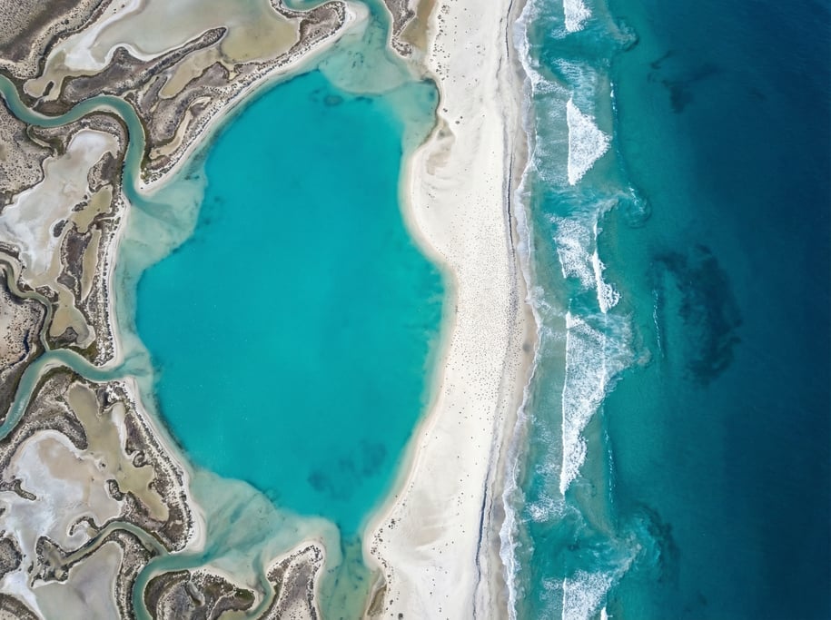 Drone view of a coastal lagoon with bright turquoise water separated from the deep blue open ocean b