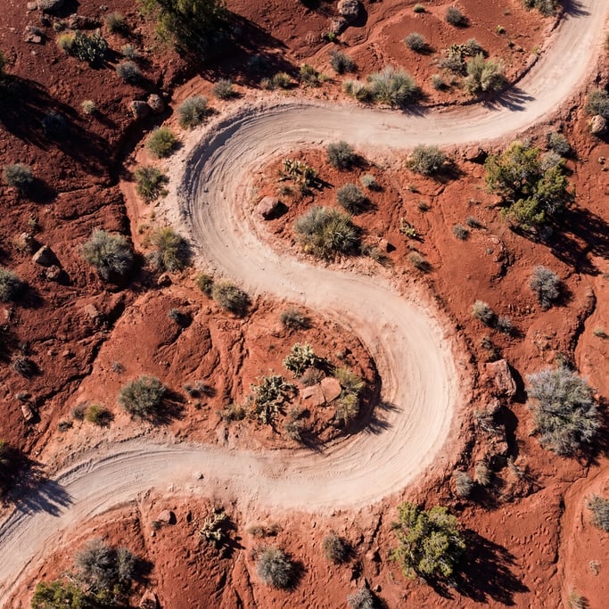 Overhead shot of a single-track trail winding through red desert terrain