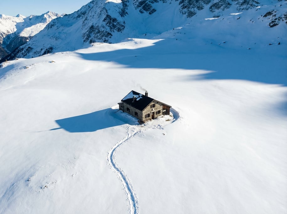 Aerial view of a mountain hut isolated on a snowy alpine meadow