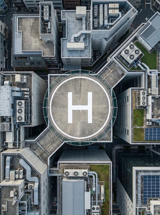 Top-down aerial of a rooftop helipad with an H marking in white on grey