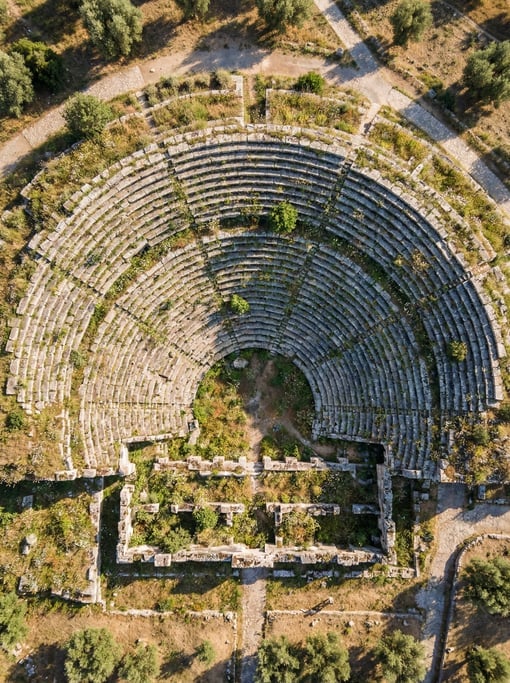 Top-down view of an ancient amphitheater ruin with concentric stone seating tiers forming a semicirc