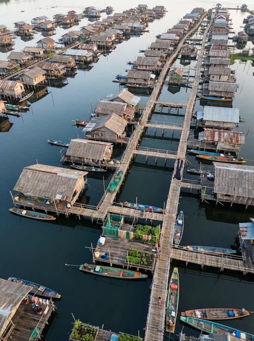 Top-down view of a floating village on a lake with wooden houses on stilts connected by walkways
