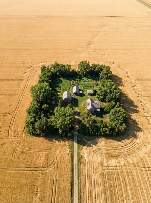 Top-down aerial of a lone farmstead on endless flat prairie