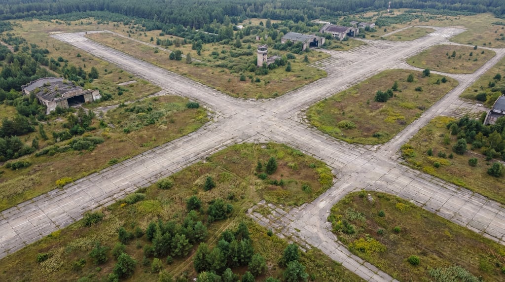 Wide drone view of an abandoned military airfield with cracked concrete runways forming a cross patt
