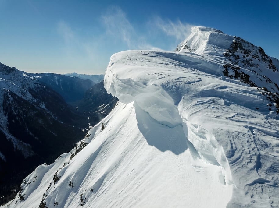 Drone view of a wind-sculpted snow cornice on a mountain ridge