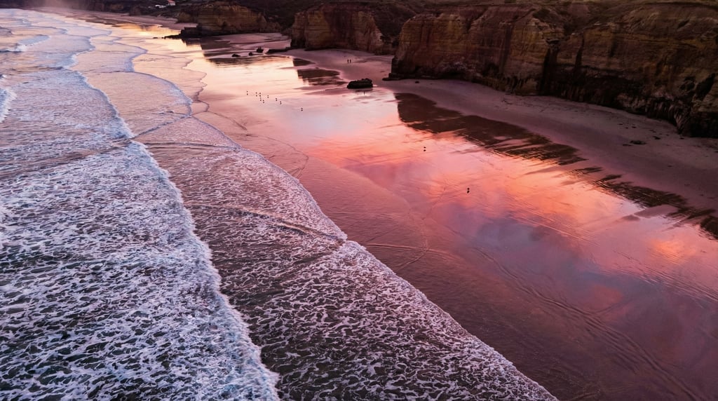 Wide aerial of a beach at sunrise with long shadows from cliff edges