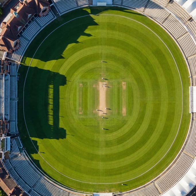 Overhead drone shot of a perfectly maintained cricket oval from above, the green pitch at center