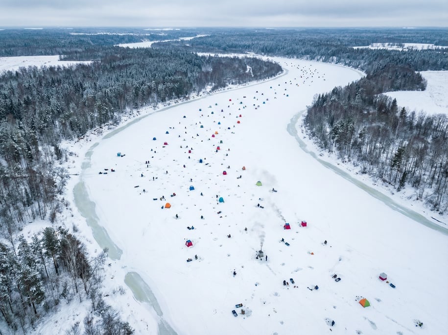 Aerial shot of a frozen river with ice fishermen sitting by small holes in the ice