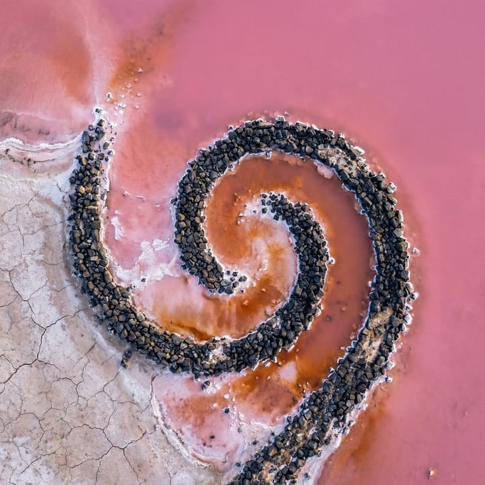 Overhead drone shot of a spiral jetty land art installation extending into a salt lake