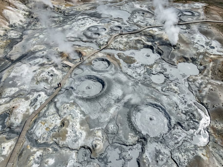 Aerial shot of a geothermal area with bubbling mud pots and steam vents creating circular formations