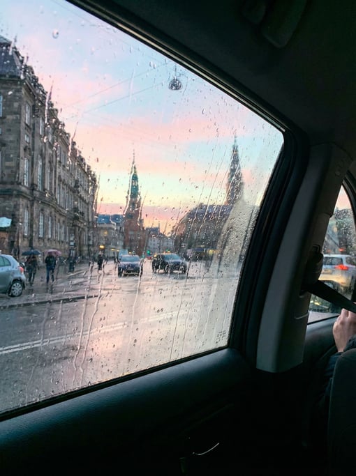 View through a rain-streaked taxi window overlooking a northern European cityscape at dawn