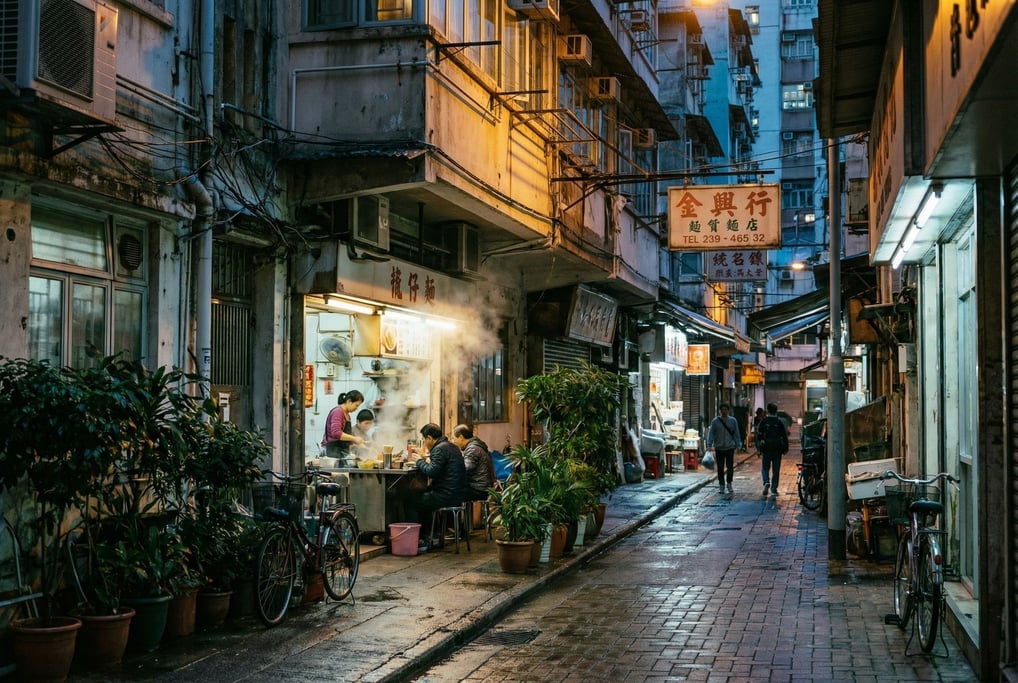 Narrow Hong Kong tong lau neighborhood street with potted plants and bicycles lining the narrow side