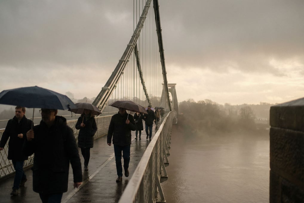 Suspension bridge spanning a wide river under overcast skies, soft even light and muted tones