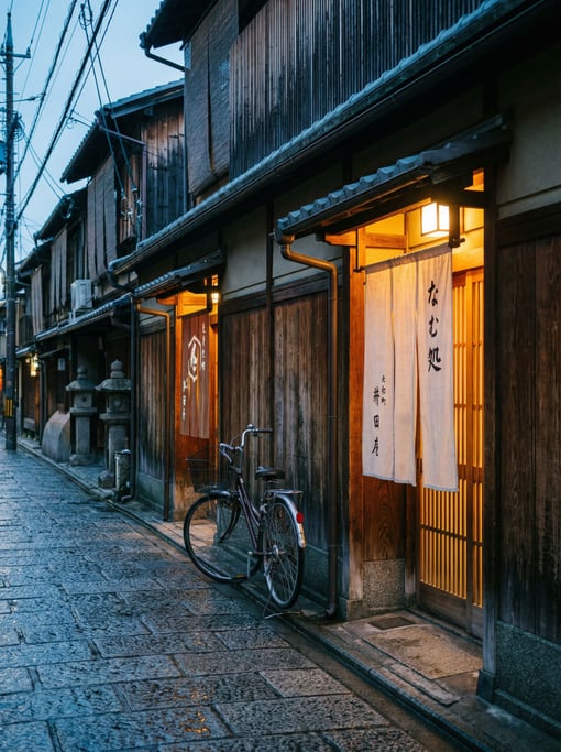 Narrow Kyoto wooden machiya street with noren curtains hanging in entries, blue hour