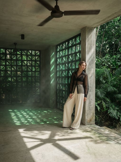 Editorial fashion photograph of a woman in a sheer black organza blouse over a black bralette and hi