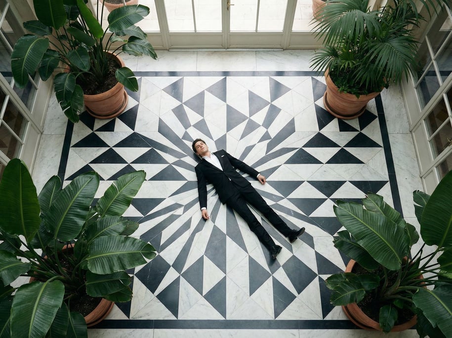 Overhead editorial fashion photograph looking straight down at a man in a black suit lying on a geom