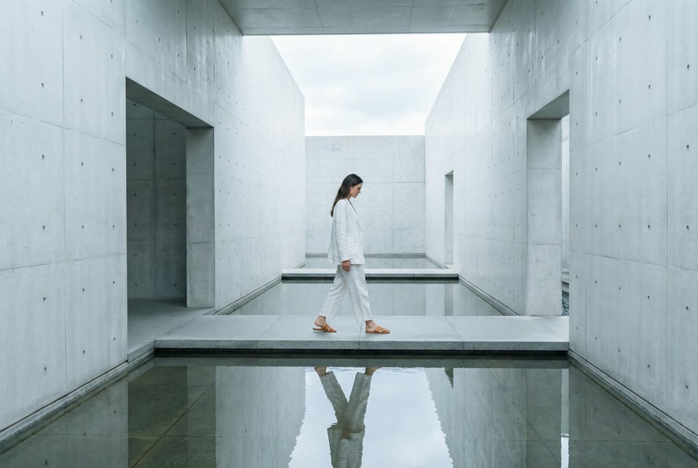 Wide environmental editorial of a woman in a white linen suit and tan leather slides walking through