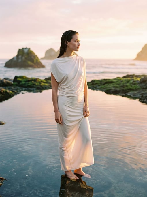 Editorial fashion photograph of a woman in a hand-draped ivory jersey dress and bare feet standing a