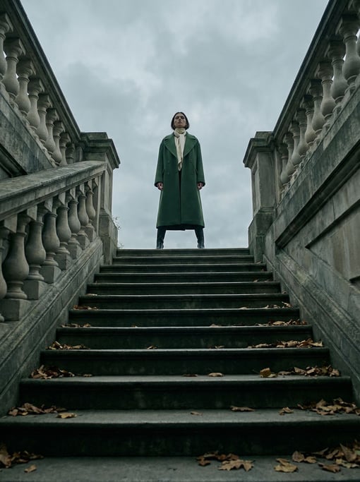 Low-angle editorial fashion photograph of a woman in a structured forest-green wool coat with wide l