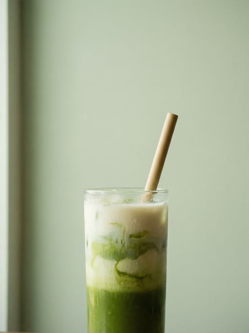A tall glass of layered iced matcha latte against a pale sage green wall