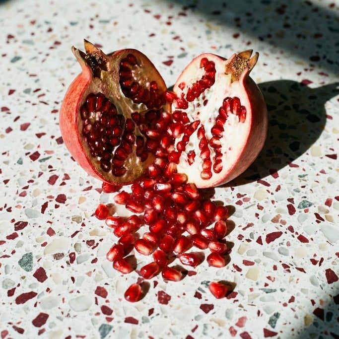 A single pomegranate split open on a terrazzo surface