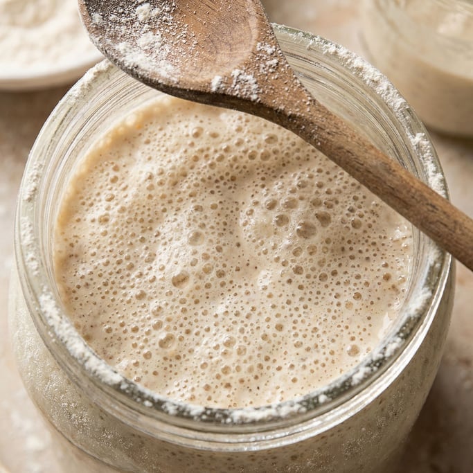 Overhead view of a bubbling sourdough starter in a wide-mouth glass jar