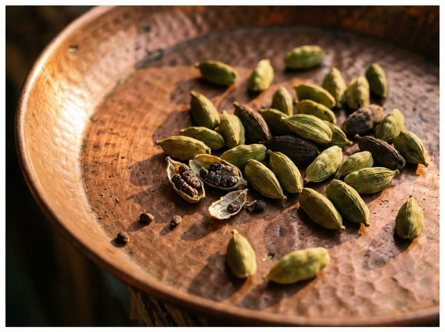 Cardamom pods — green and black varieties — scattered across a copper plate